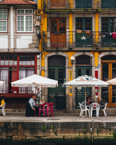Ribeira district in Porto, Portugal, with colorful buildings along the Douro River, people dining at outdoor cafes.