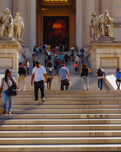 The grand entrance of The Metropolitan Museum of Art in NYC, visitors climbing the steps on a bright sunny day.